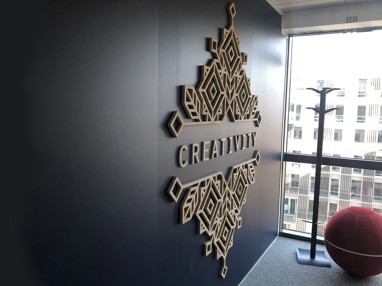 Motif géométrique et mot Creativity en bois découpé au laser sur mur gris